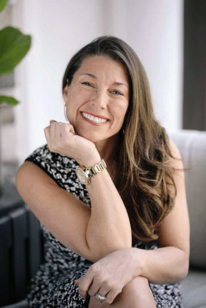Smiling woman in a black and white patterned dress, resting her chin on her hand, promoting wellness and chiropractic care at HFC Wellness.